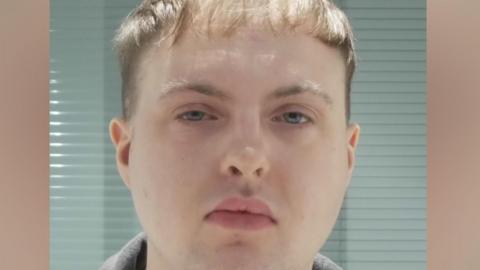 Police custody photograph of Tom Heckley. He has short brown hair and is wearing a grey hooded top.