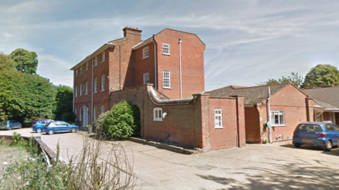A three-storey red brick building with cars parked outside. 