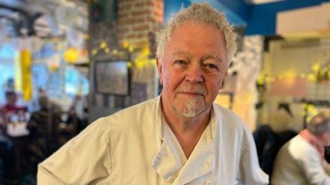 Pete Zulu in chef uniform at the Black Horse pub. He has short white hair.