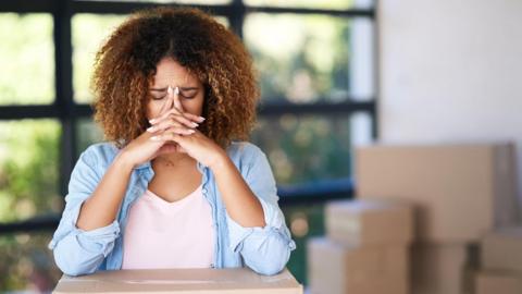 A woman with her head in her hands surrounded by boxes