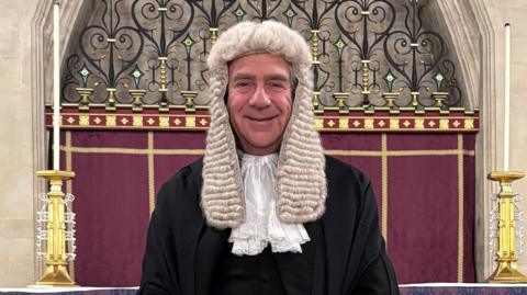 Judge Martyn Levett wearing a judicial wig and traditional, black and white judicial attire. He is smiling and looking into the camera.
