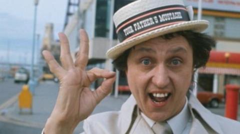 Sir Ken Dodd with straw boater on Blackpool prom with the tower in the background.