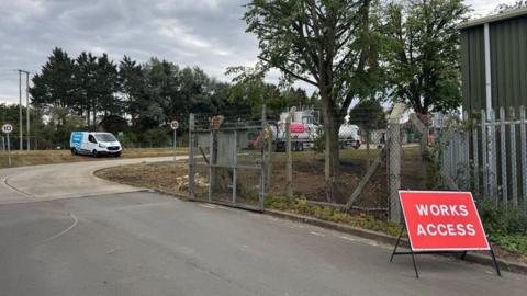 A view of the Wheatley Sewage Treatment Works site where a tank is parked and can be seen behind a metal fencing. There is a red sign for "Works access".