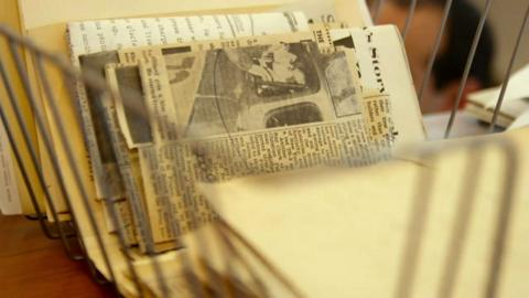Newspapers in a wire basket in a scene from the documentary OBIT