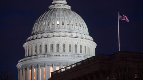 US Capitol buiding seen at night, with a US flag in the foreground