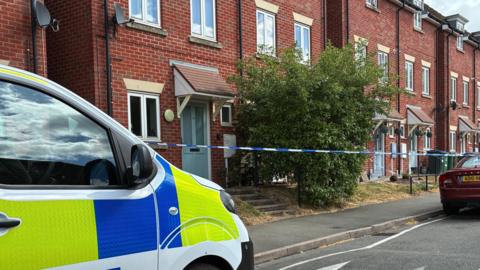 a residential street with a police cordon in place. A police van is parked on the road