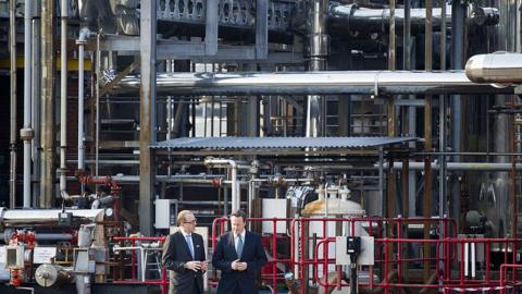 David Cameron (right) talks to CEO of GlaxoSmithKline, Andrew Witty, during a visit to the Ulverston site. They are both wearing dark suits. Mr Cameron has dark hair while Mr Witty has fair hair and glasses.