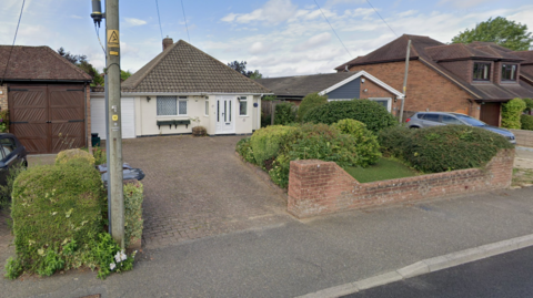 Garden and white home with triangle roof and green trees in front garden