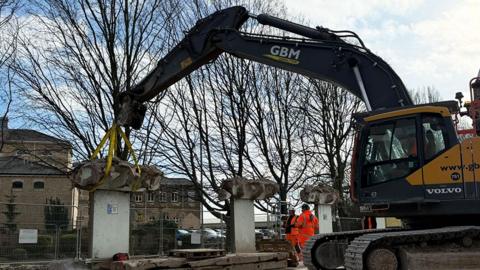 A crane removes the artwork from the demolished car park with two workers in high visibility outfits