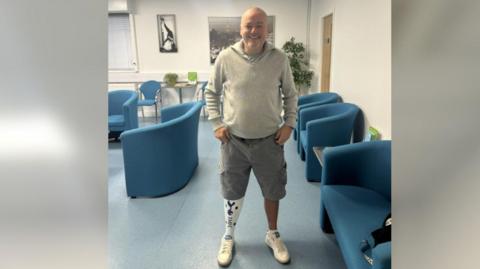 Wayne Hatton standing in what appears to be a waiting room with blue chairs. He is wearing shorts and has a white prosthetic leg.