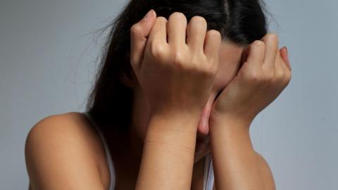 A young, distressed girl holds her hands in front of her face.