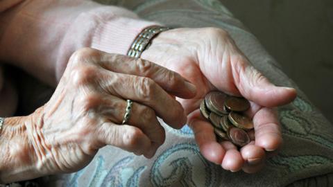 A pair of an elderly woman's hands holding coins. One hand has a wedding ring on a finger and she wears a wristwatch. 