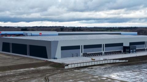 A large grey warehouse, with a grey cloud in the background.