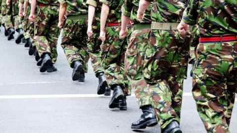 An anonymous photograph of British soldiers in uniform marching, framed so that we do not see their heads.