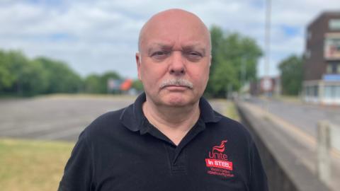 Mr Foster wears a black top with "Unite in Steel" red logo on it.