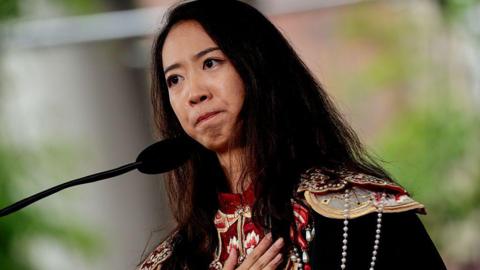 Yurong Luanna Jiang, dressed in a black and red top with strings of pearls and what appear to be shoulder decorations in gold, looks emotional as she delivers the Graduate English Address during Harvard University's 374th Commencement on 29 May