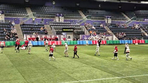 An indoor American Football match, with a team in white playing a team in red