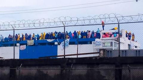 Venezuelan prisoners gather in protest on the roof of the Judicial Detention Centre in Barinas, Venezuela on 24 May, 2026. The inmates are wearing jumpsuits, some of them yellow, others blue. They have hung hand-drawn signs from the roof.