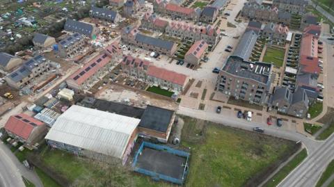 An aerial view of some newly built houses on land by the former Oakfield campus. Some of the houses have solar panels and cars parked in the driveway. Some of the houses appear to be unfinished.