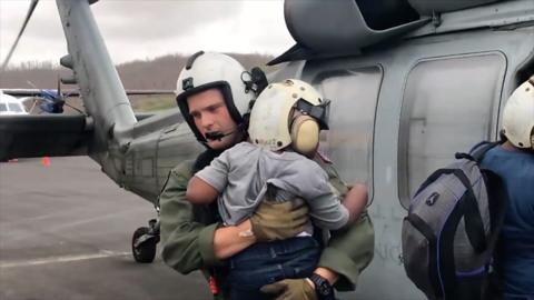 US Navy officer carries young boy off a helicopter