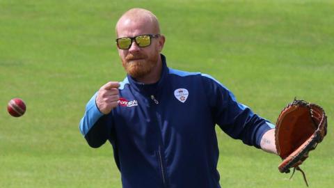 Graeme Welch in sunglasses and wearing a baseball mitt throws the ball during a fielding routine