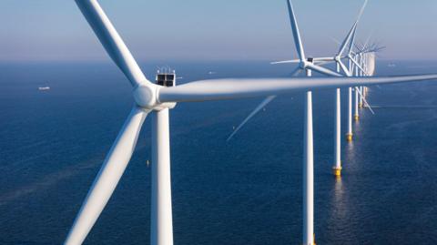 Stock image of offshore wind turbines - tall, windmill-like structures rising from the sea.