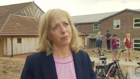 Liz Jarvis MP is looking towards the camera. She is wearing a pink shirt and blue jacket. 