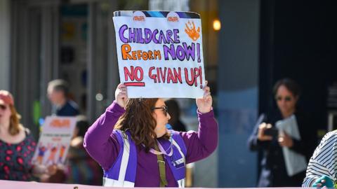 Woman holding a sign that reads 'childcare reform now! No Givan up!'