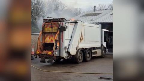 Fire and smoke emerges from the roof of a white bin lorry