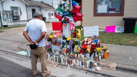 A man observes a makeshift memorial for Lorenzo Salgado Araujo, which features candles, ballons, and the Mexican flag.