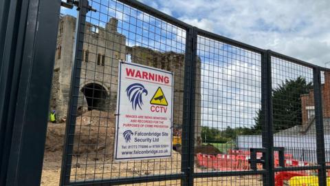 Newark Castle gatehouse seen through the fence of the construction site - with a security warning prominently displayed