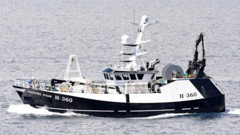 The trawler Guiding Star moving from right to left across frame. The sea is calm and grey.