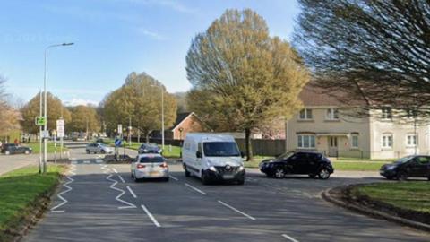 Several cars negotiate a junction and pedestrian crossing on a residential street