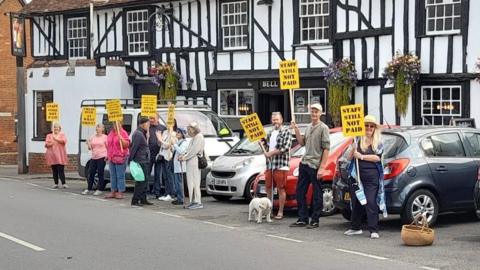 Men and women standing outside the Bell Hotel, in Clare, holding yellow placards which read: "Staff still not paid". 