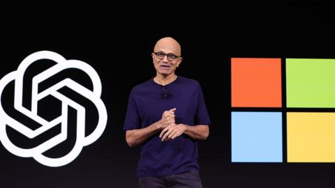 Microsoft boss Satya Nadella talking on stage in front of the OpenAI and Microsoft logos