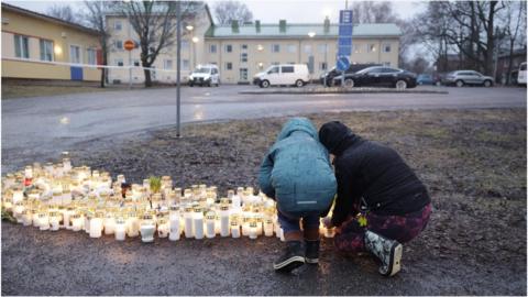 Two people leave candles in front on the school in Vantaa