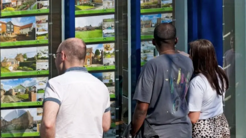 three people looking in an estate agents window