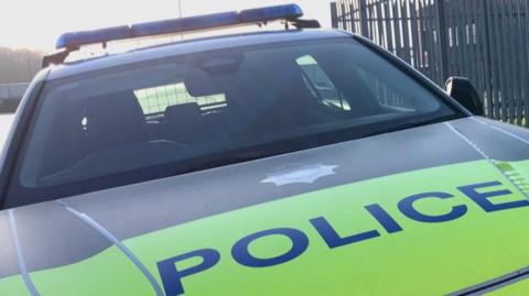 A police car parked in front of grey railings.