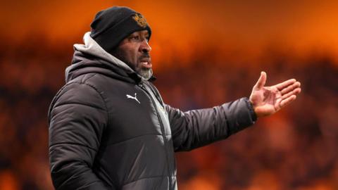 Darren Moore waving some instructions to his players from the touchline dressed in puffer coat and beanie 