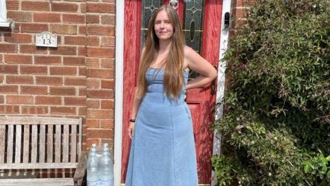 Amy Cox wearing a blue dress in front of a red brick house with a red door