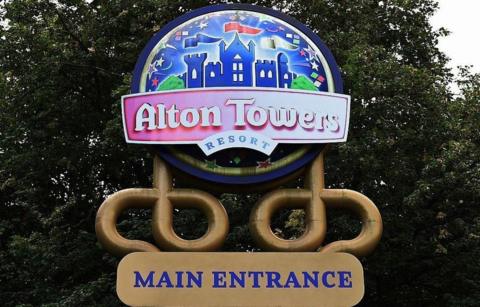 Sign at the entrance of Alton Towers showing the logo for the resort, a badge saying "Alton Towers resort" and underneath "Main entrance" against a backdrop of trees