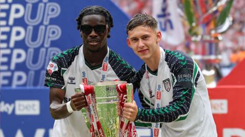 Eliezer Mayenda and Chris Rigg hold the 2025 Championship play-off final trophy