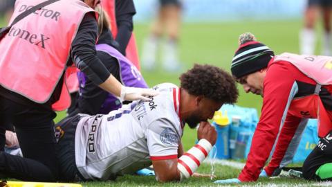 Andy Onyeama-Christie receives treatment after injuring his ankle against Harlequins