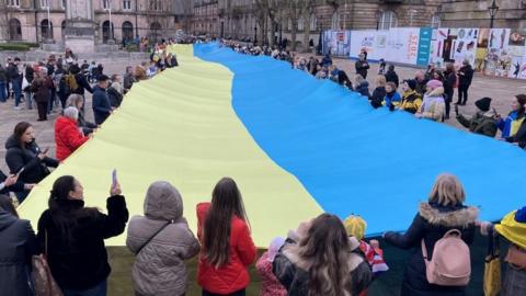 a crowd gathers around the Ukrainian flag