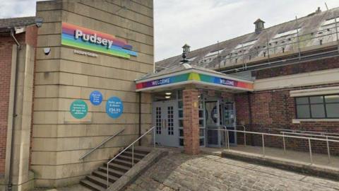 The outside of Pudsey Leisure Centre, as denoted by signage over the entrance. The front door is at the top of a set of steps.