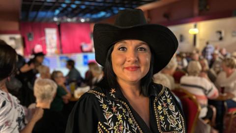 Becky Sainty wearing a cowboy hat smiling at the camera 