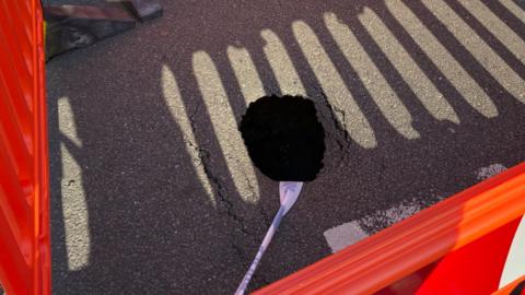 A sinkhole within a square-shaped cordoned-off area surrounded by red barriers.