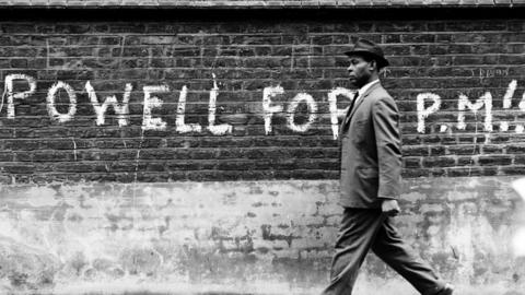 Man walking past graffiti stating "Powell For PM" (prime minister), 1st May 1968