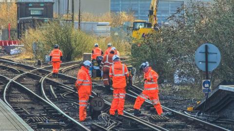 A group of Network Rail engineers dressed in bright orange protective clothing work on the railway tracks at Three Bridges railway station in Crawley, UK.