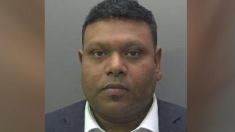 Shajahan wearing a blue blazer and white shirt in his custody photo.